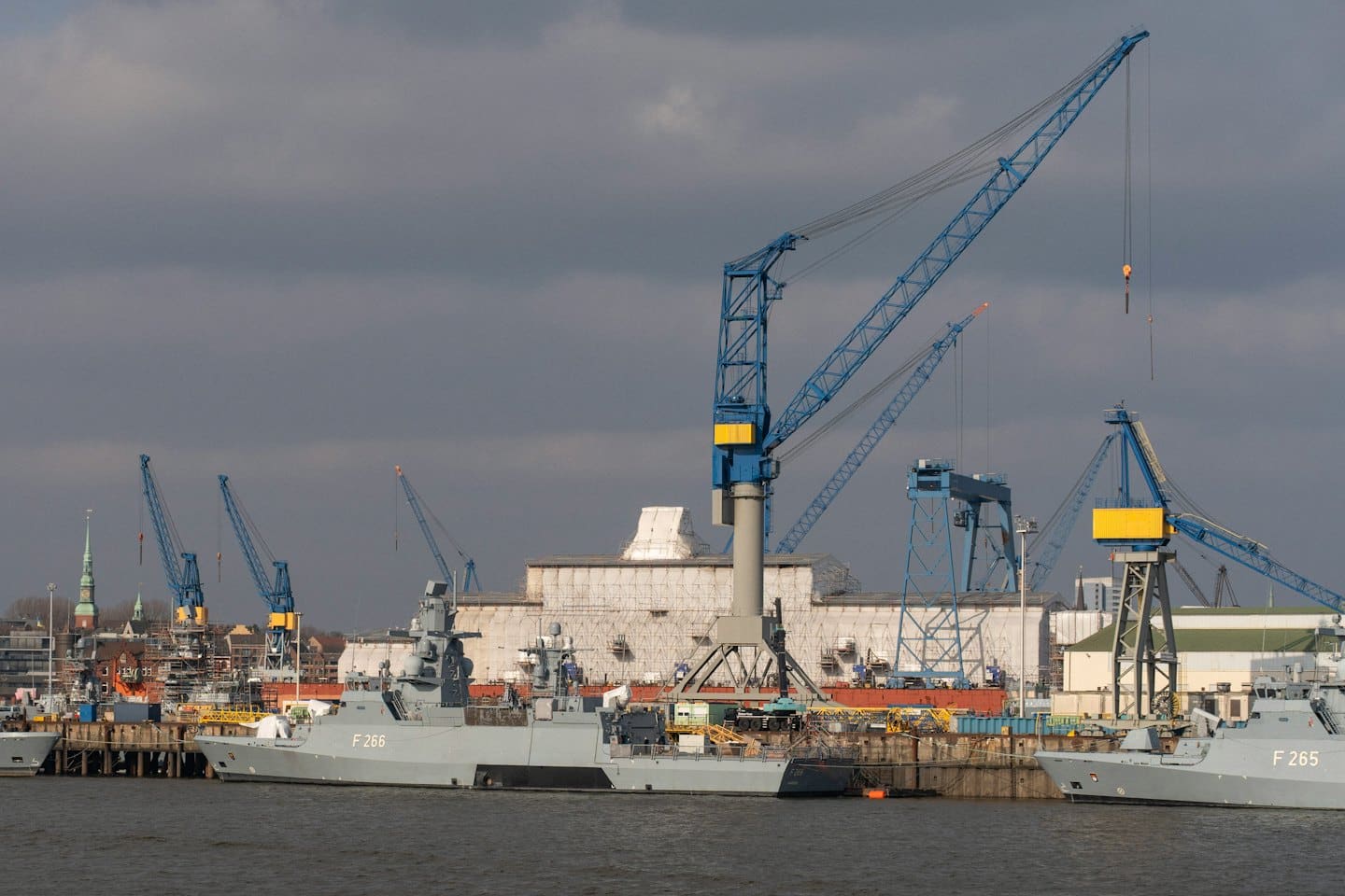 Navi militari attraccate in un cantiere navale con grandi gru a portale.