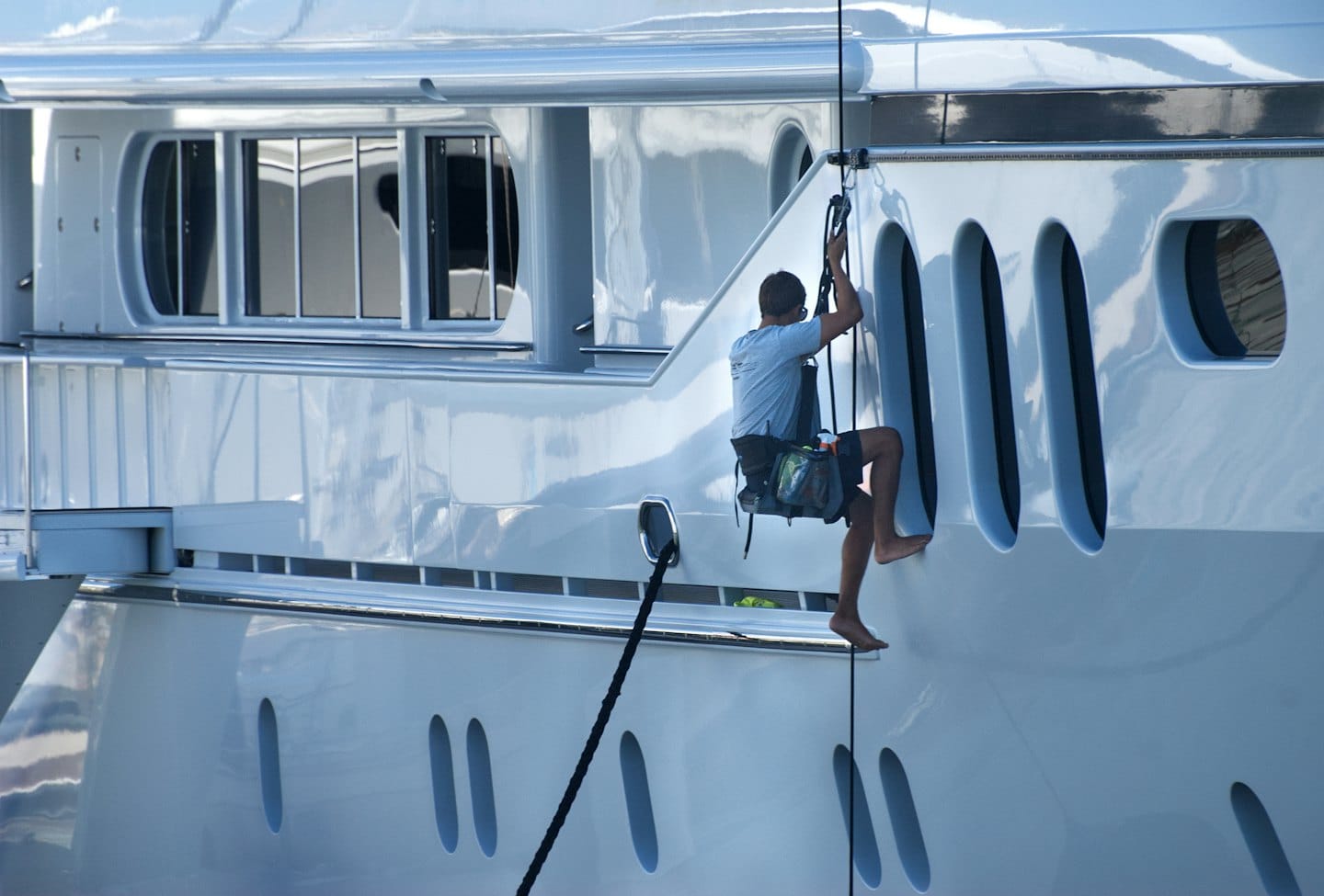 Operaio addetto alla manutenzione che pulisce il fianco di un grande yacht di lusso.